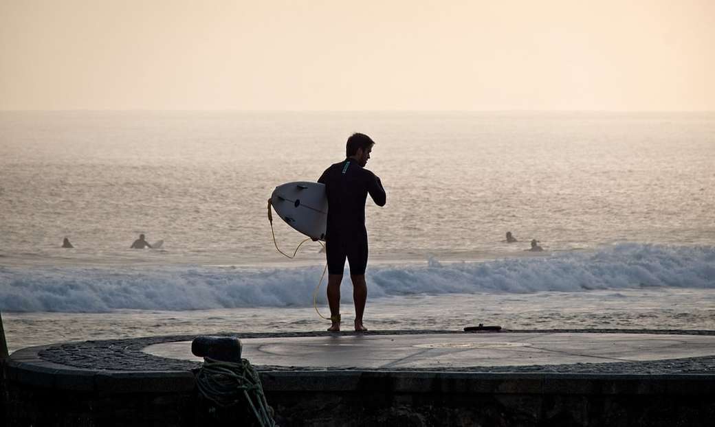 mężczyzna trzyma deskę surfingową w pobliżu morza puzzle online