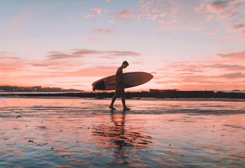 mężczyzna trzyma deskę surfingową spaceru w pobliżu morza puzzle online