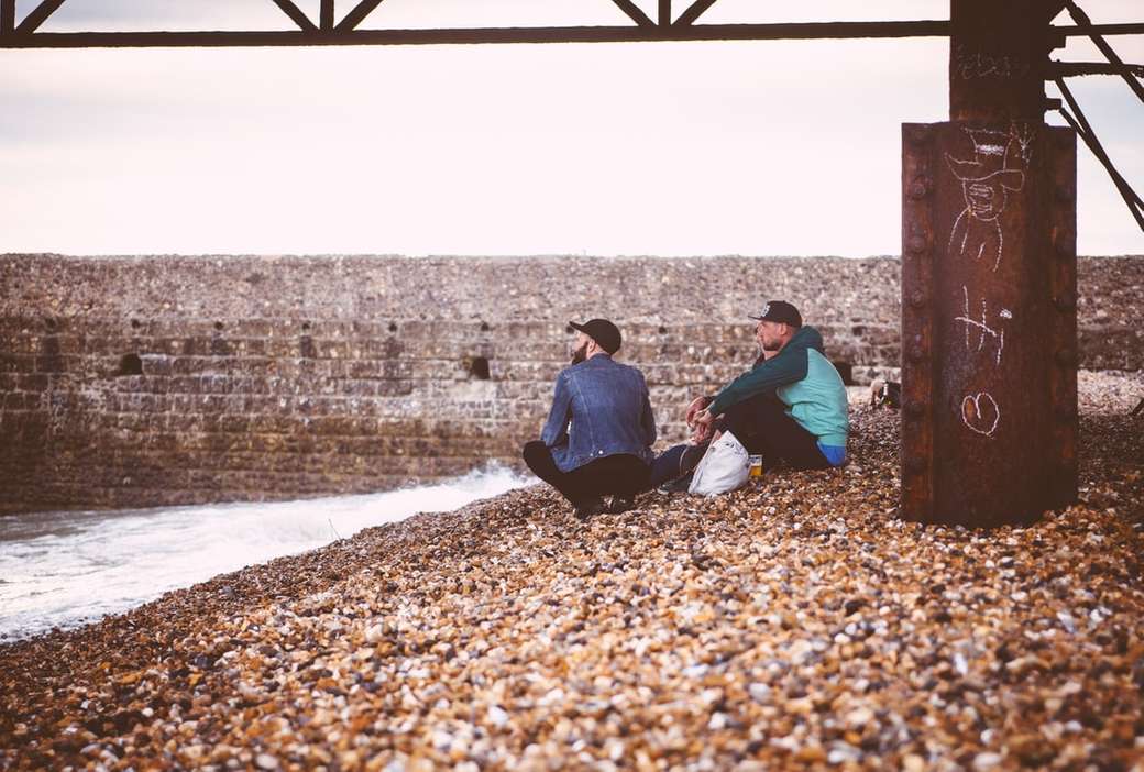 Mężczyźni siedzący na kamienistej plaży puzzle online