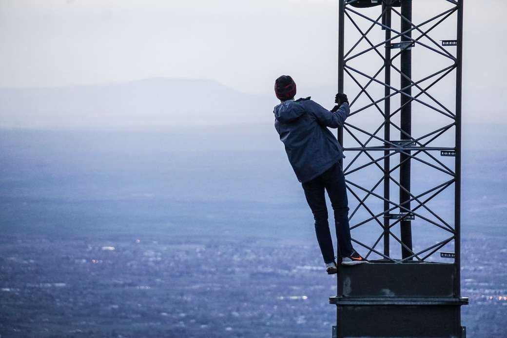 człowiek wspinający się na wieżę w pobliżu budynków w ciągu dnia puzzle online