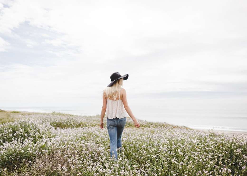 kobieta w czarnym kapeluszu spacerująca po polu kwiatowym w ciągu dnia puzzle online