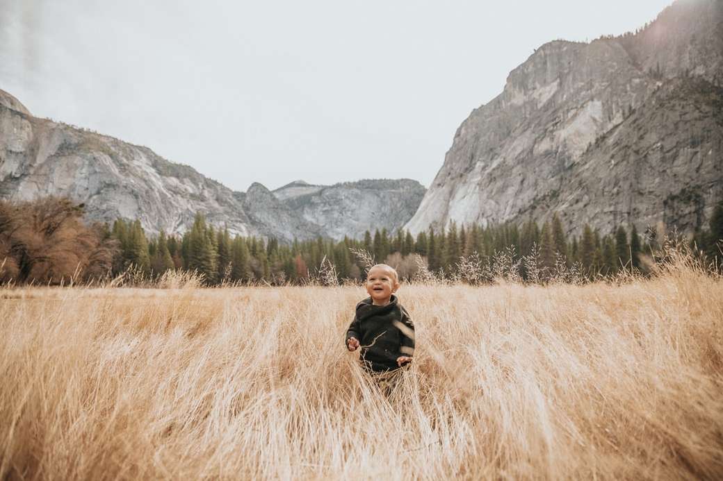 chłopiec w czarnej kurtce stanąć na brązowej trawie w pobliżu góry puzzle online