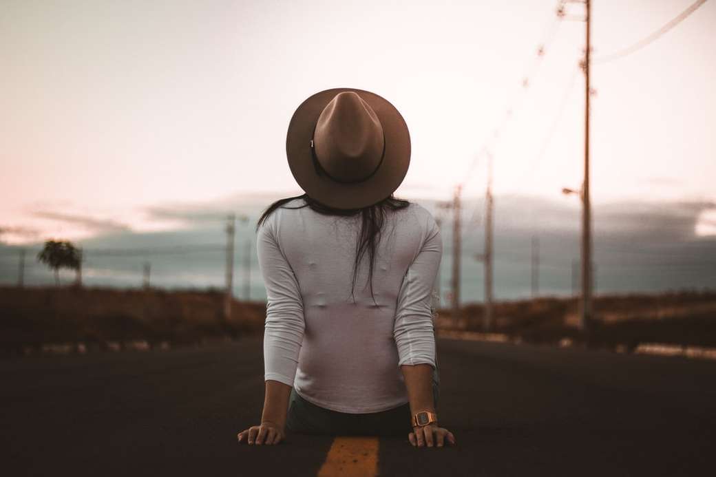kobieta siedzi na drodze ubrana w białą koszulę i brązowy kapelusz puzzle online