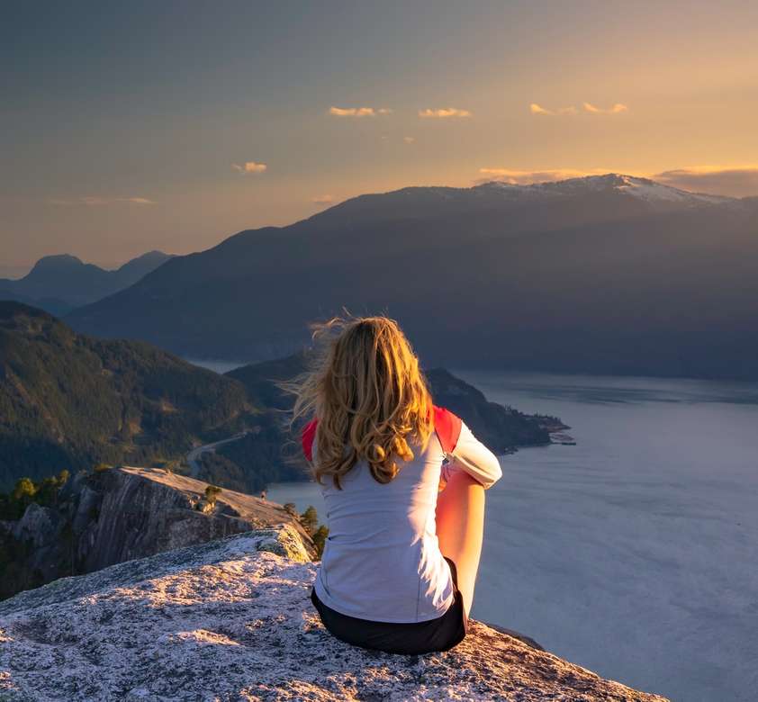 Kobieta siedzi na szczycie góry o zachodzie słońca. puzzle online