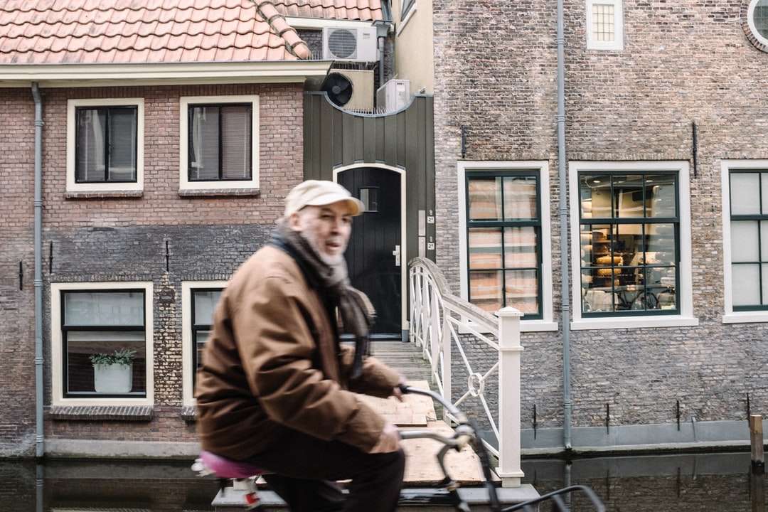 mężczyzna w brązowej kurtce siedzący obok betonowego budynku puzzle online