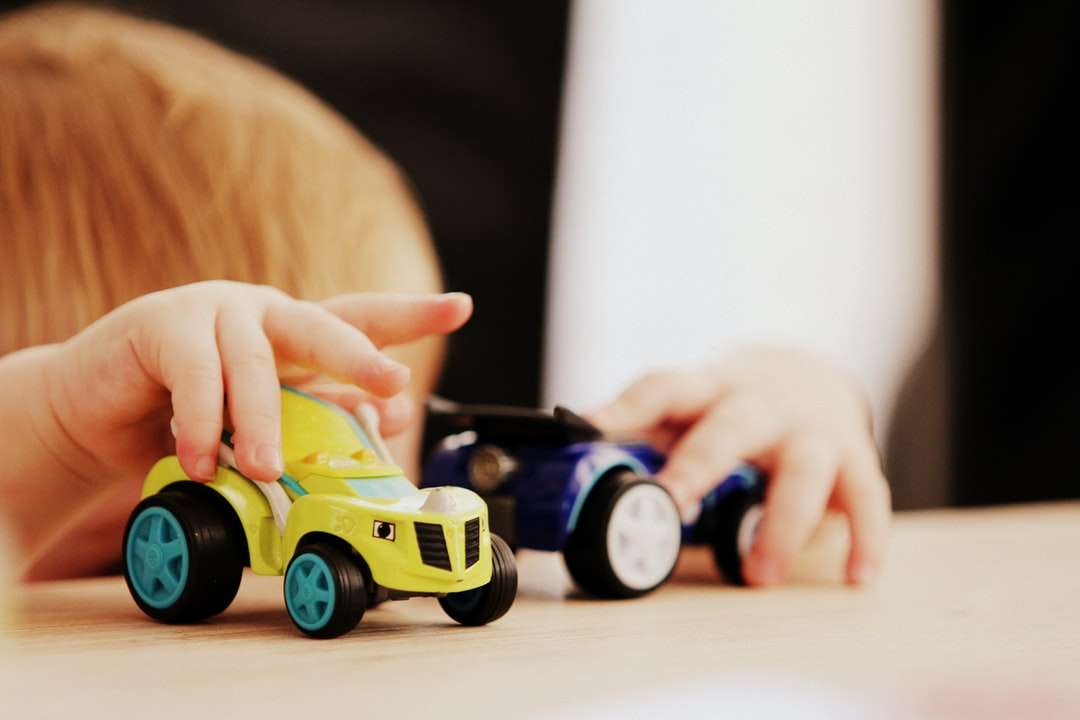 dziecko bawi się dwoma plastikowymi zabawkami samochodowymi w różnych kolorach puzzle online