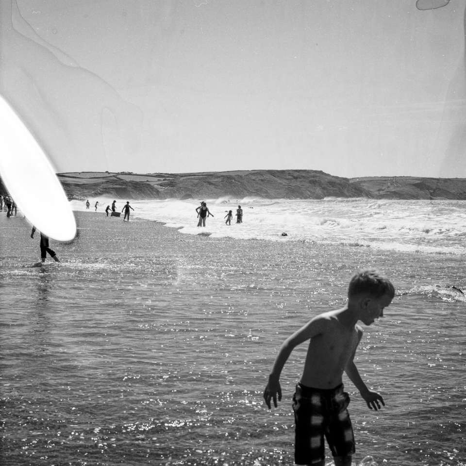zdjęcie w skali szarości chłopca trzymającego deskę surfingową na plaży puzzle online