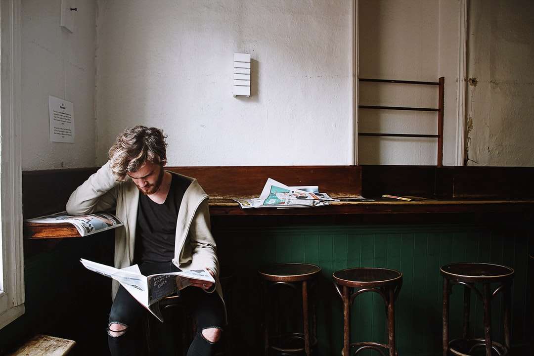 mężczyzna siedzi na stołku barowym, trzymając gazetę puzzle online