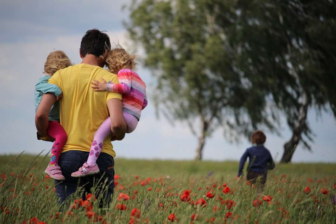 mężczyzna prowadzący do dziewcząt na polu czerwonych płatków kwiatu puzzle online