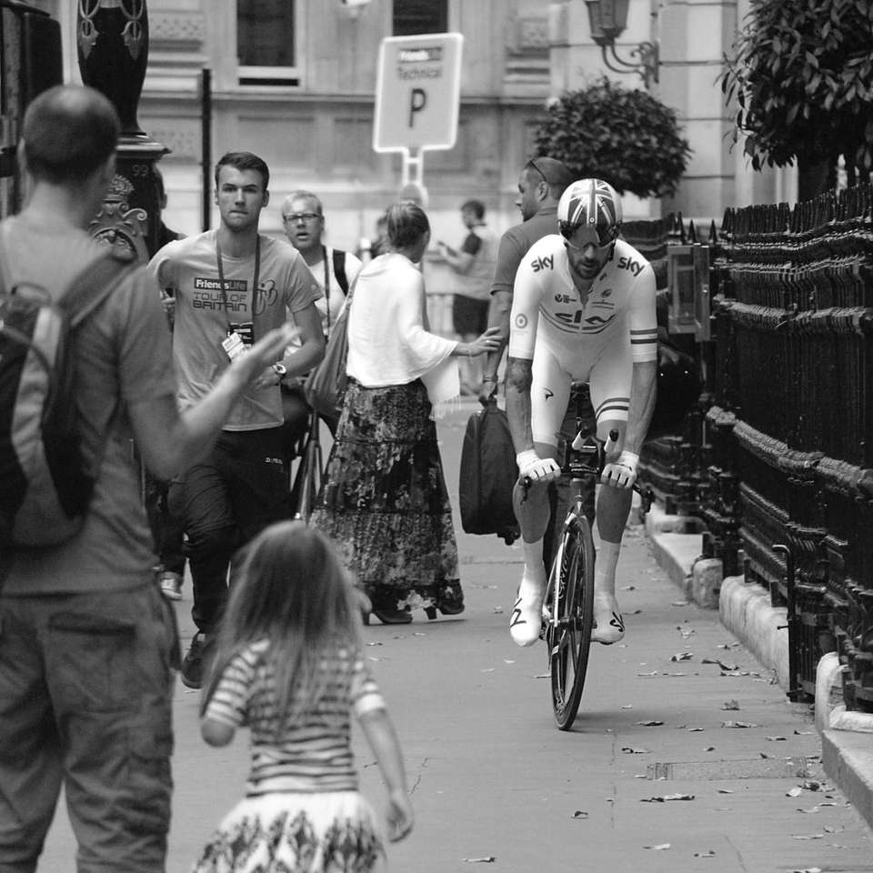 zdjęcie w skali szarości przedstawiające mężczyznę jadącego na rowerze obok grupy ludzi puzzle
