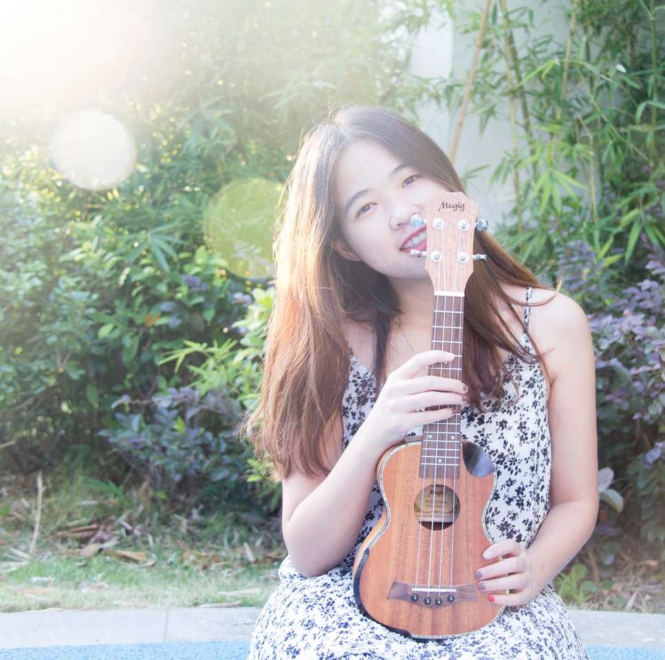 uśmiechnięta kobieta trzyma ukulele w pobliżu zielonych roślin puzzle online