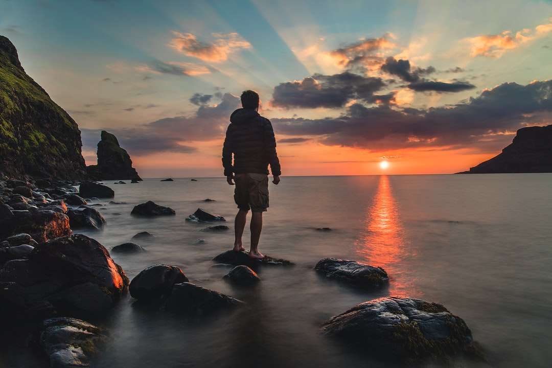 człowiek stojący na kamieniu patrząc na zachód słońca puzzle online