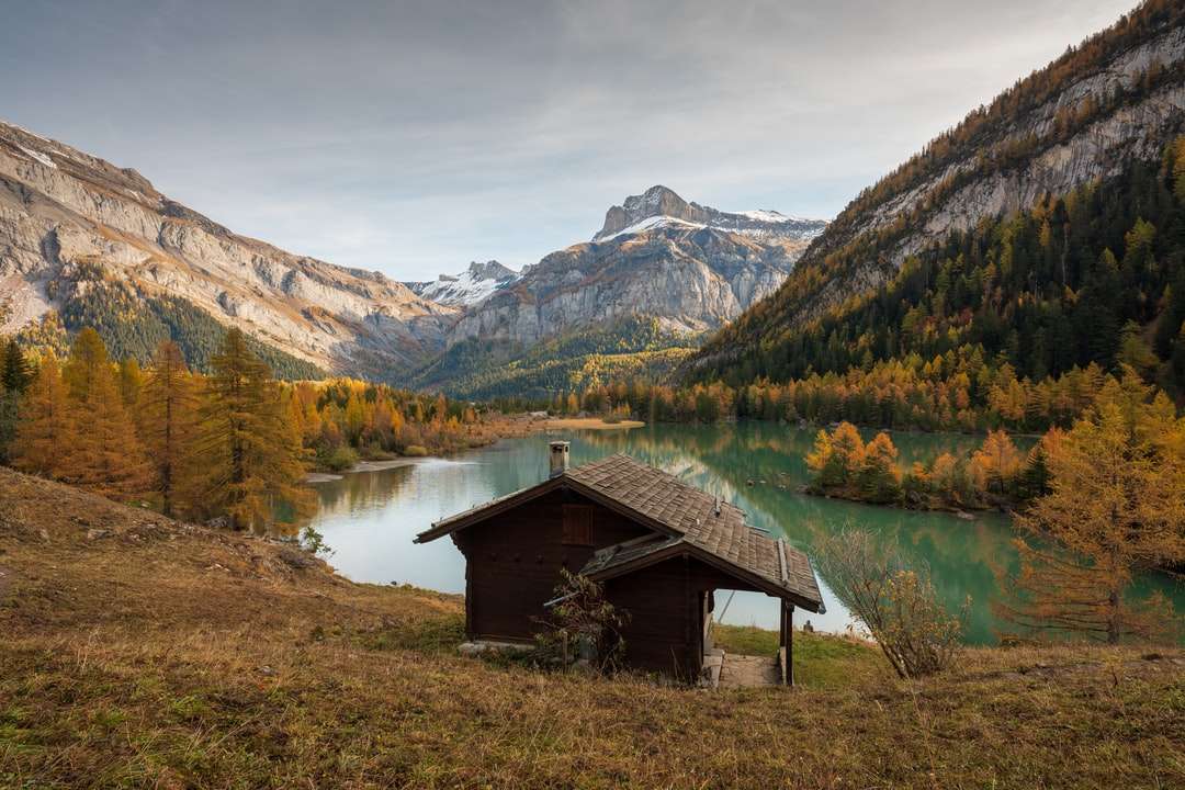 brązowy drewniany dom nad jeziorem w pobliżu zielonych i brązowych gór puzzle online