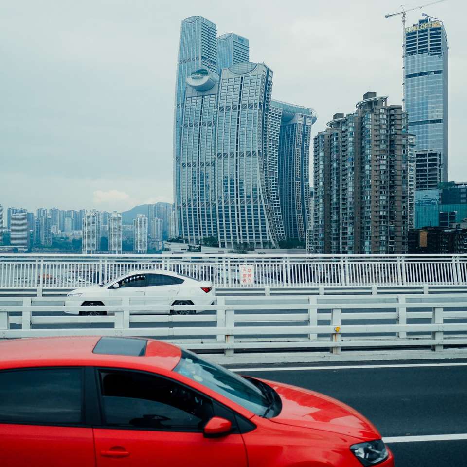 czerwony samochód na drodze w pobliżu budynków miejskich w ciągu dnia puzzle online