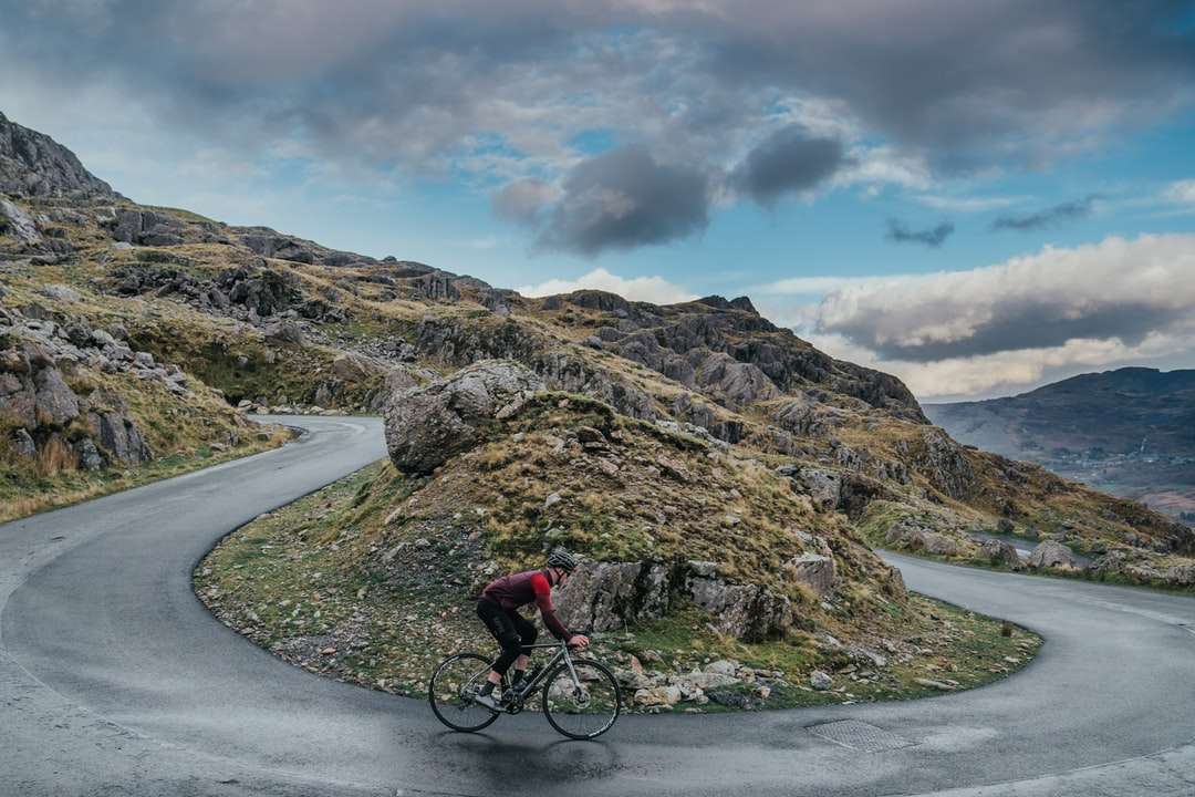 człowiek w czerwonej kurtce, jazda na rowerze na drodze w pobliżu góry puzzle online