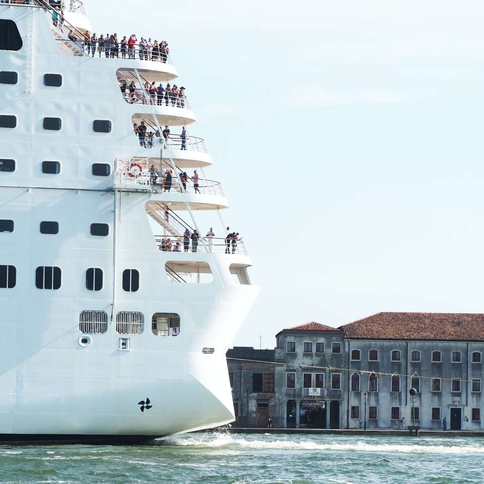 biały statek na wodzie w pobliżu brązowego betonowego budynku puzzle online