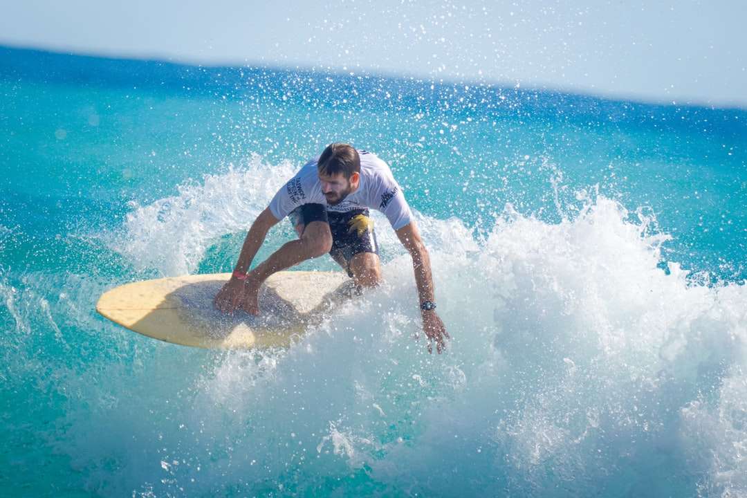mężczyzna w białej koszulce i niebieskich spodenkach, surfing na falach morskich puzzle online