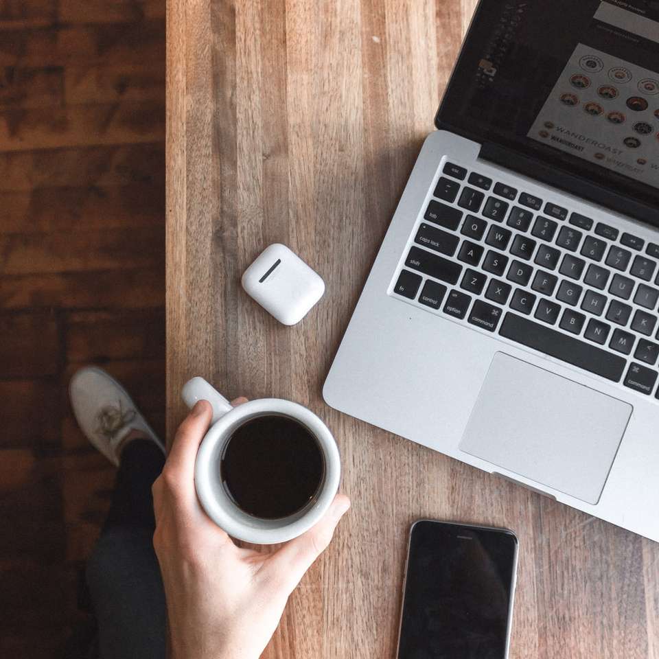 osoba trzymająca filiżankę kawy obok szarego laptopa puzzle online