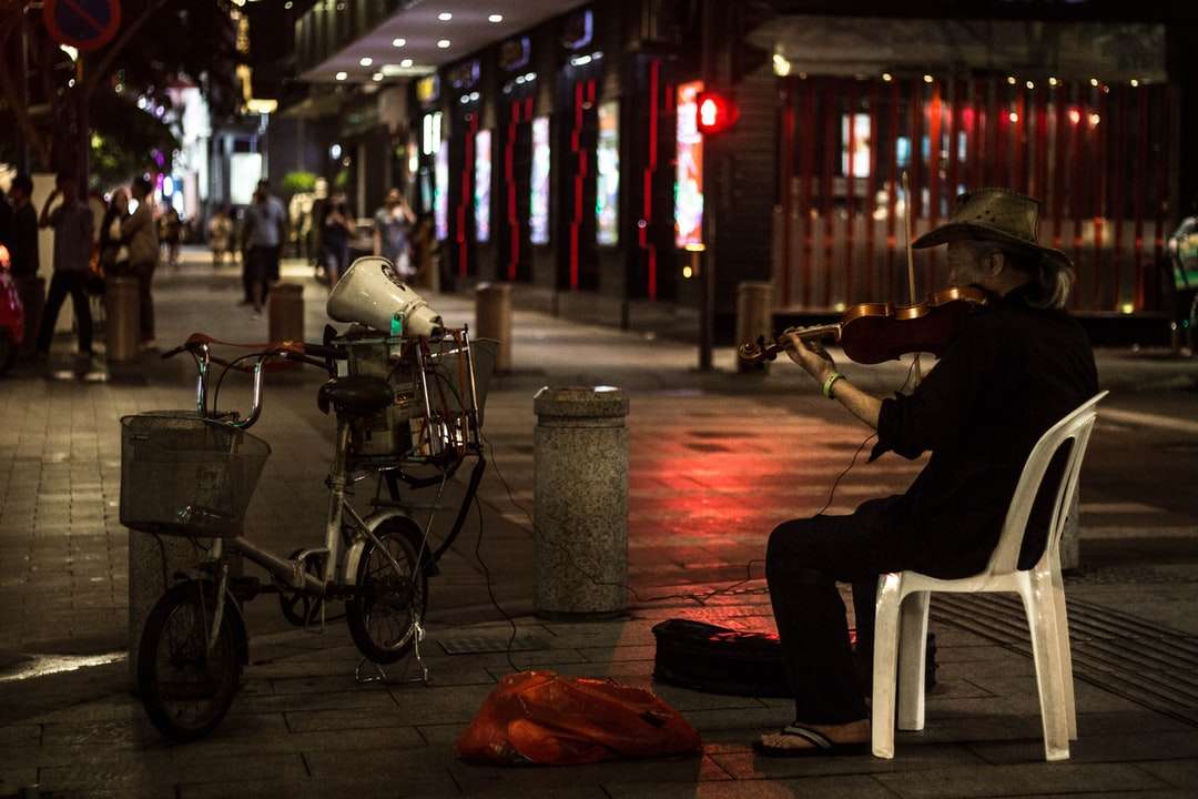 mężczyzna w czarnej koszuli siedzi na białym plastikowym krześle w pobliżu drogi puzzle online