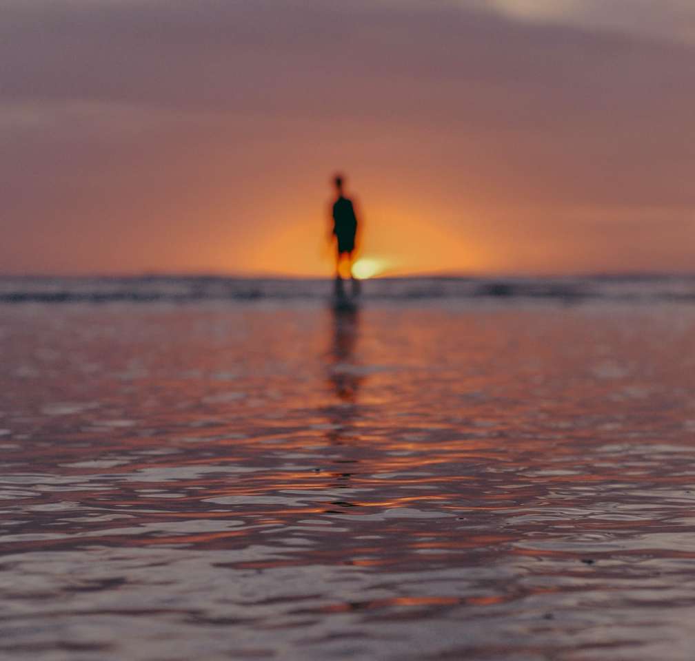 osoba stojąca na wodzie morskiej podczas zachodu słońca puzzle online