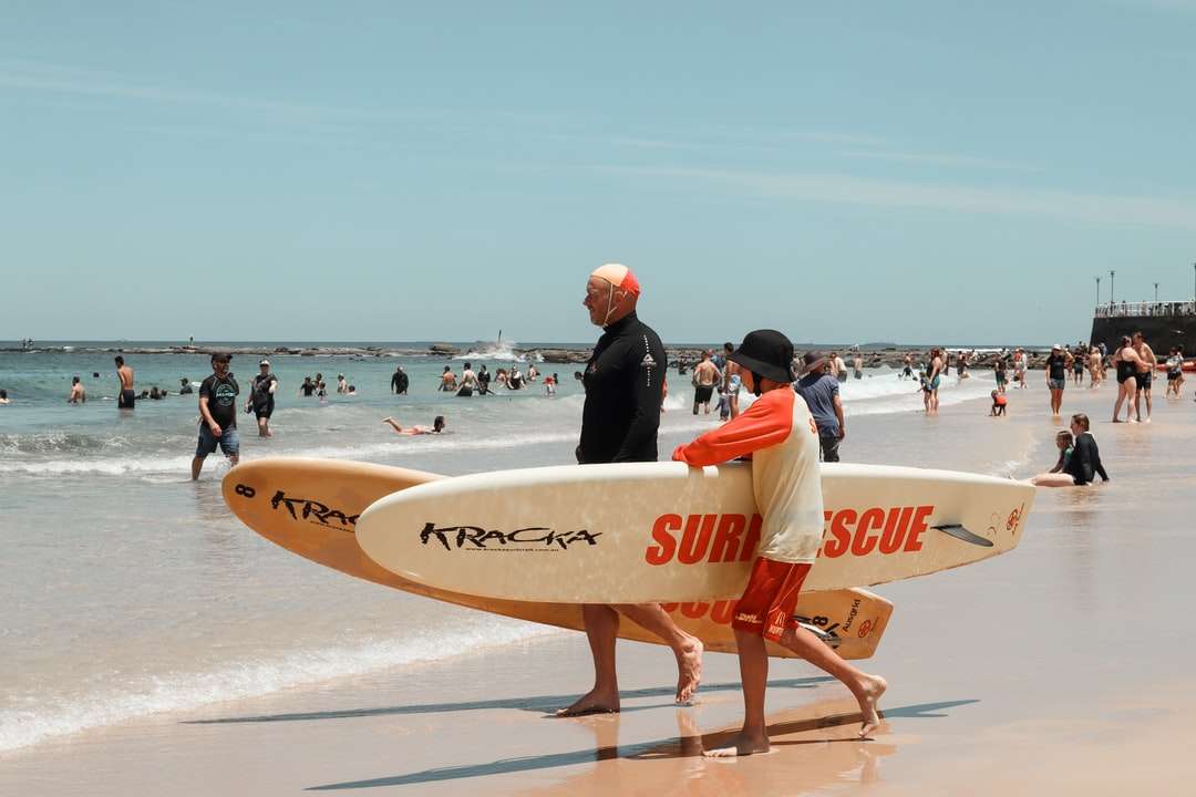 mężczyzna w czarnym kombinezonie, trzymając białą deskę surfingową puzzle online
