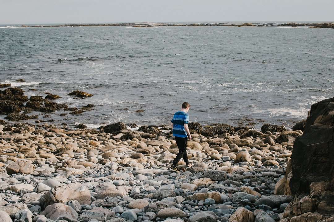 chłopiec w niebieskiej koszuli i czarnych spodniach chodzenia po skalistym brzegu puzzle online