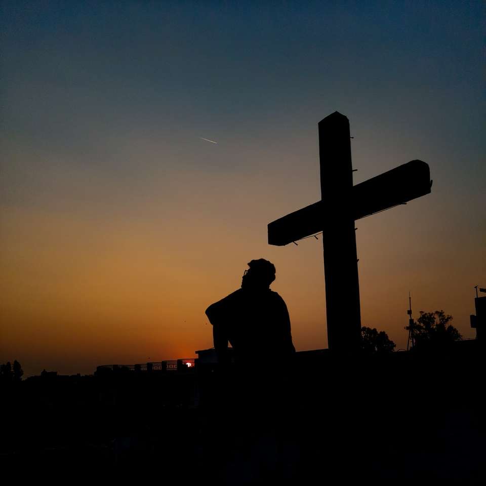 sylwetka człowieka stojącego w pobliżu krzyża podczas zachodu słońca puzzle online