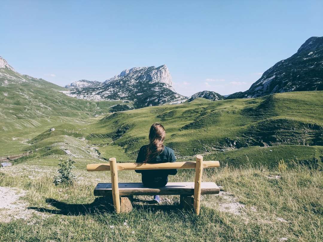 kobieta siedzi na brązowej drewnianej ławce na zielonej trawie puzzle online
