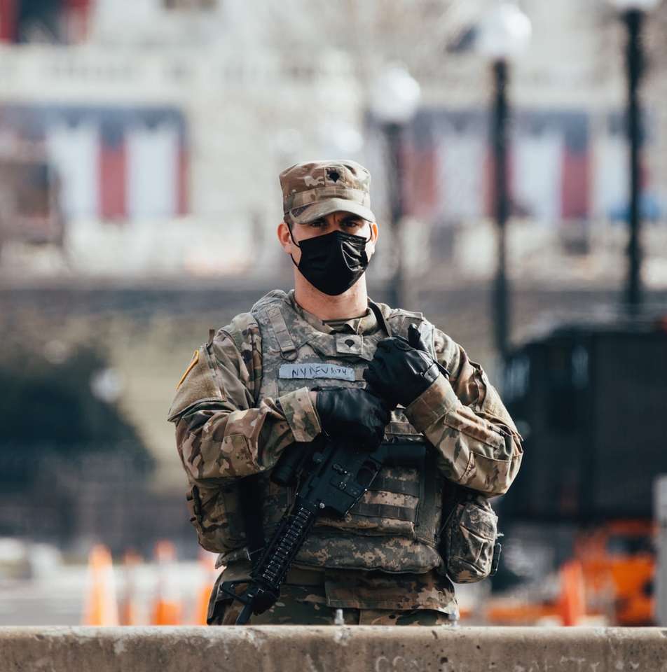 Hombre en uniforme de camuflaje negro y marrón sosteniendo un rifle rompecabezas