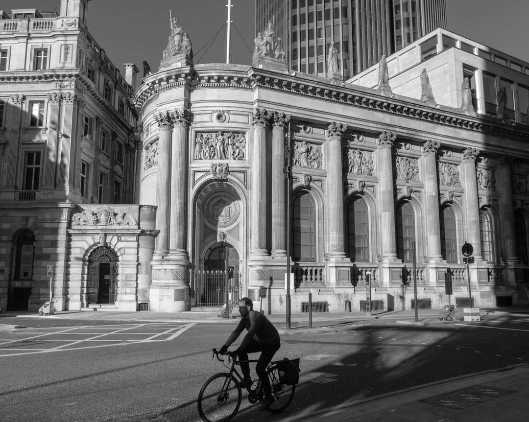 grayscale photo of man riding bicycle on road near building jigsaw puzzle