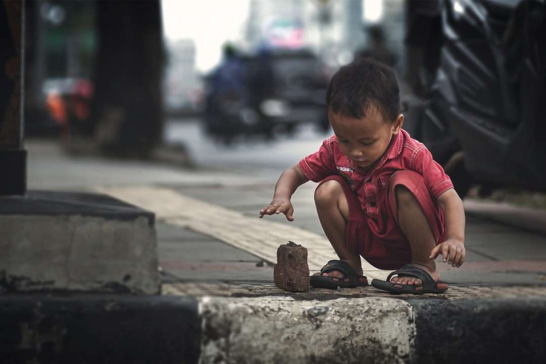 chłopiec w czerwonej koszulce z okrągłym dekoltem siedzi na betonowym chodniku puzzle online