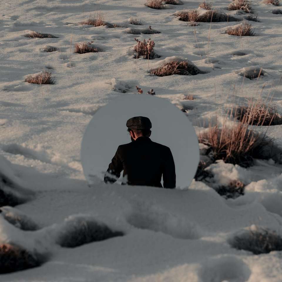 osoba w czarnym płaszczu siedzi na ziemi pokrytej śniegiem puzzle online