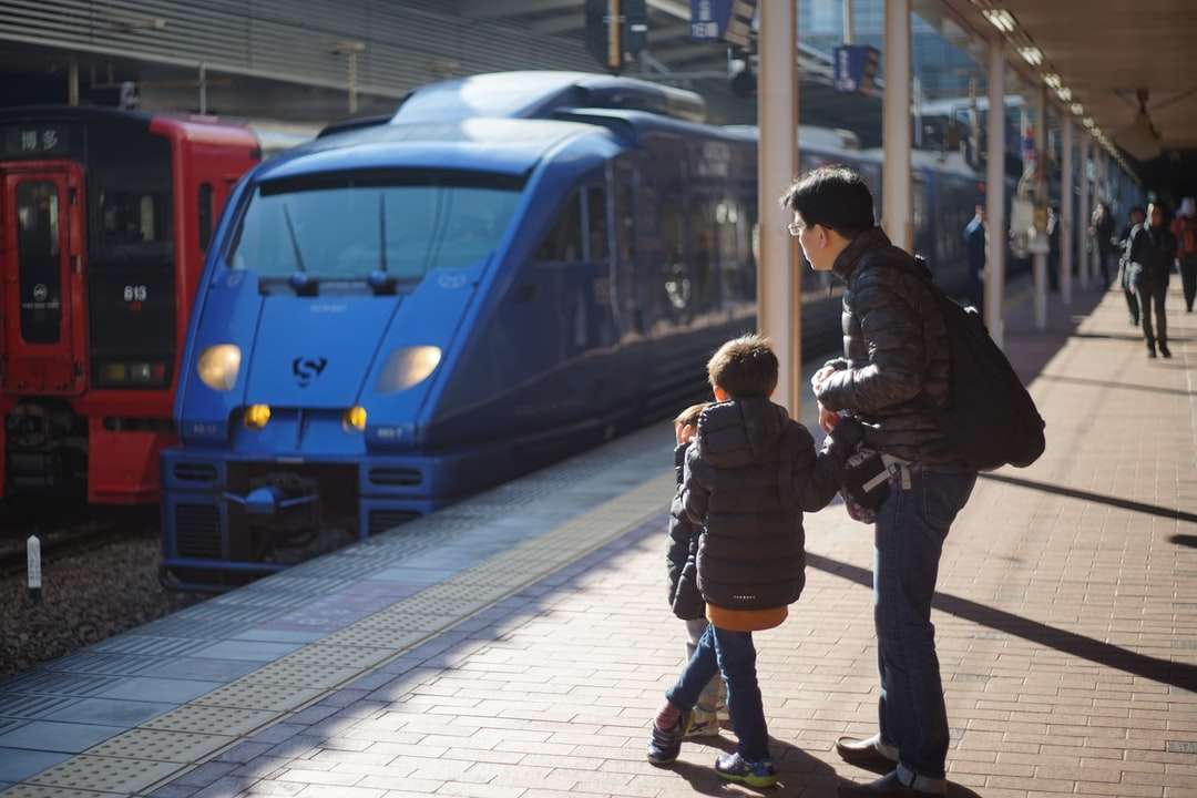 mężczyzna w czarnej kurtce stojący obok niebieskiego pociągu puzzle online