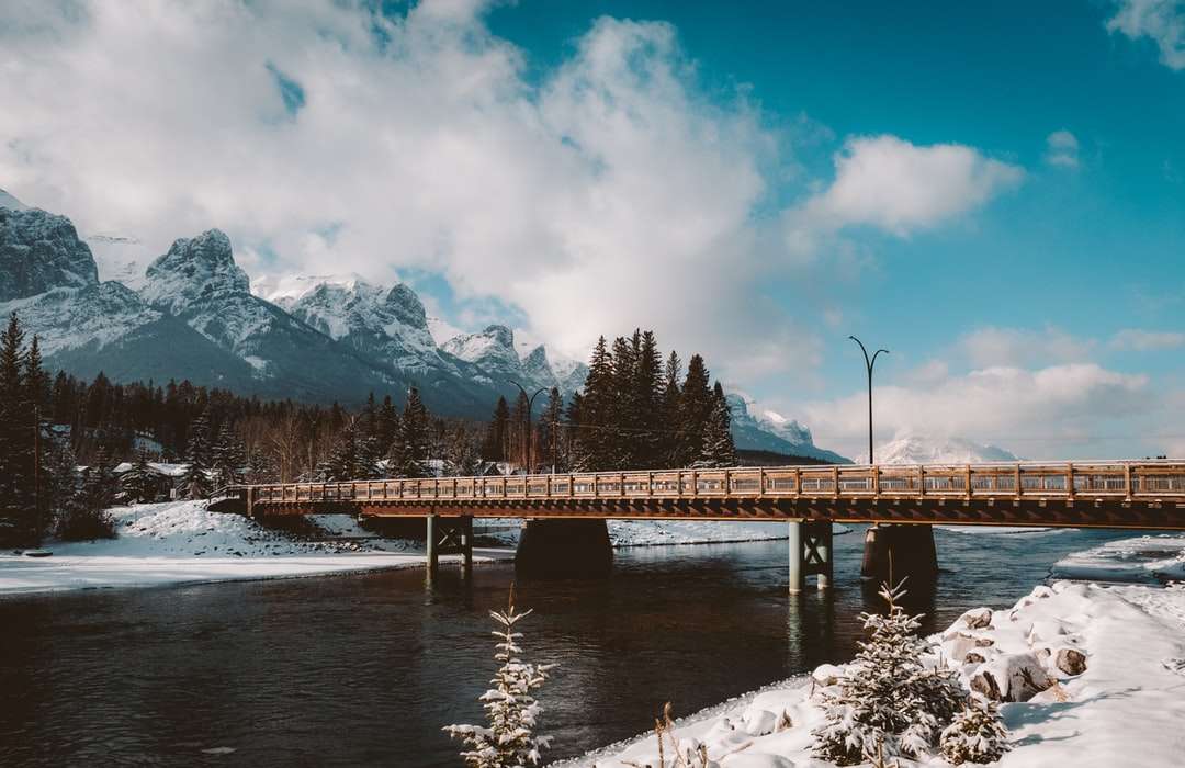 brązowy drewniany most nad rzeką w pobliżu góry pokryte śniegiem puzzle online