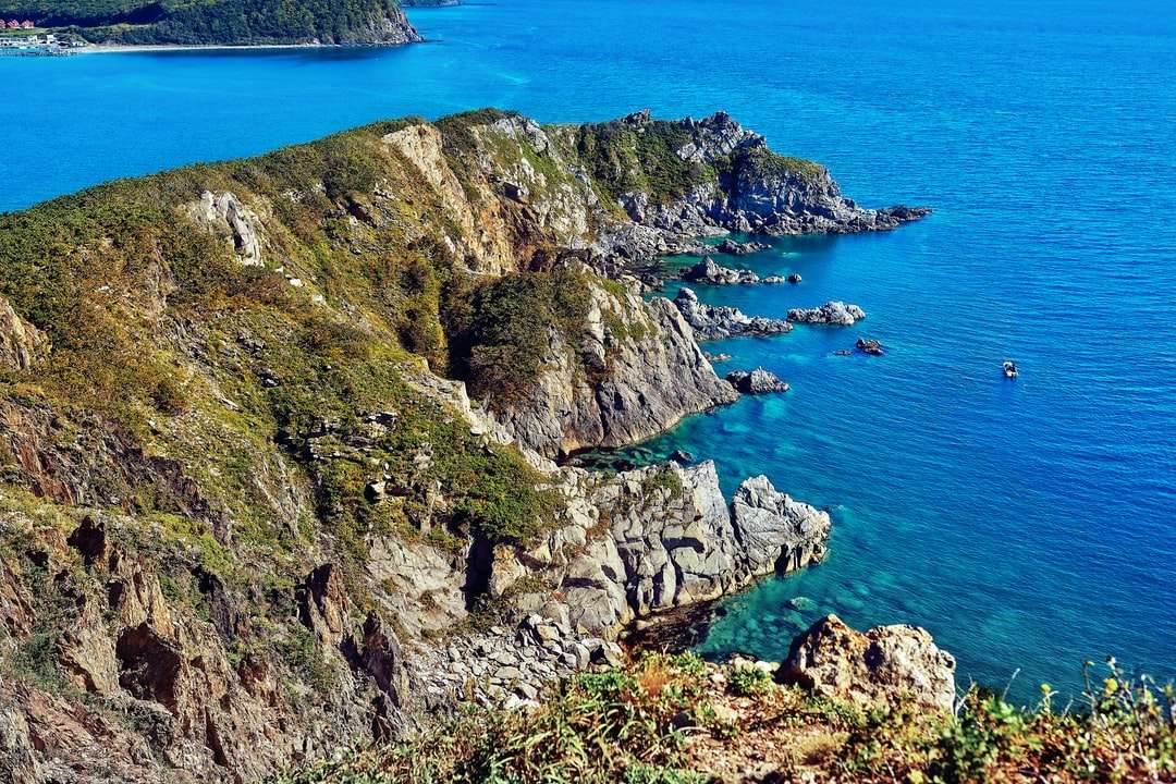 zielona i brązowa formacja skalna nad błękitnym morzem puzzle online