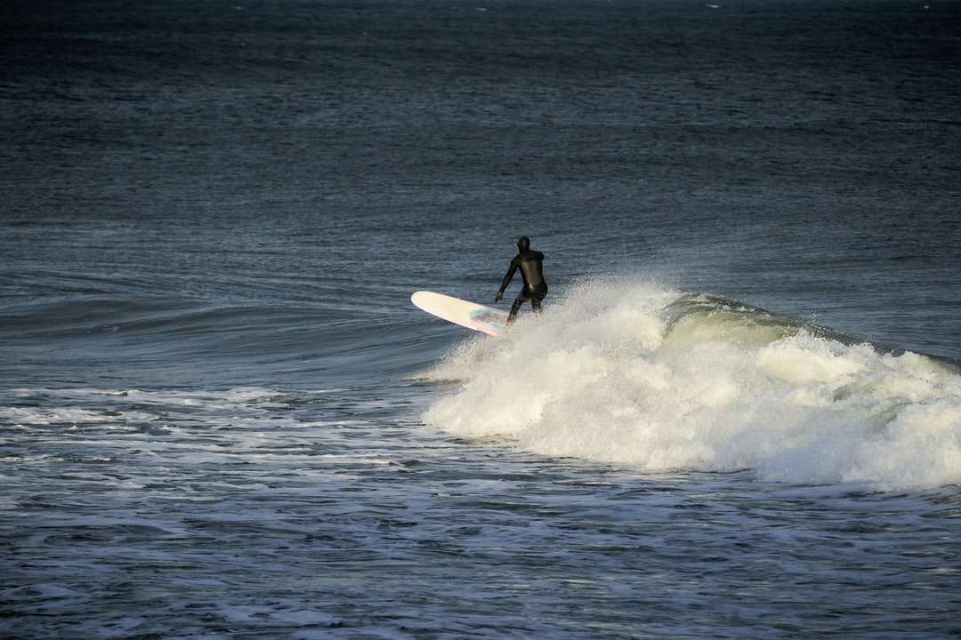 mężczyzna w czarnym kombinezonie, jazda na białej desce surfingowej na falach morskich puzzle online