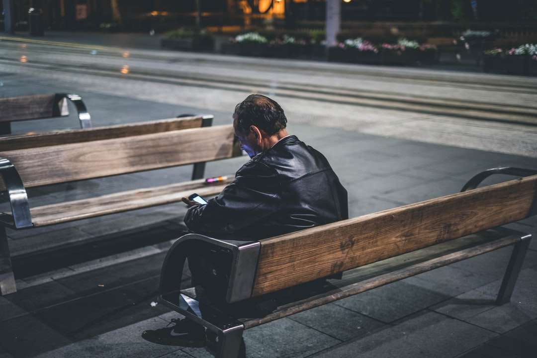mężczyzna w czarnej kurtce siedzi na brązowej drewnianej ławce puzzle online