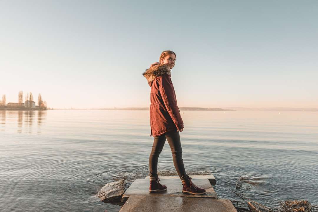 kobieta w czerwonym płaszczu stojąc na skale w pobliżu morza w ciągu dnia puzzle online