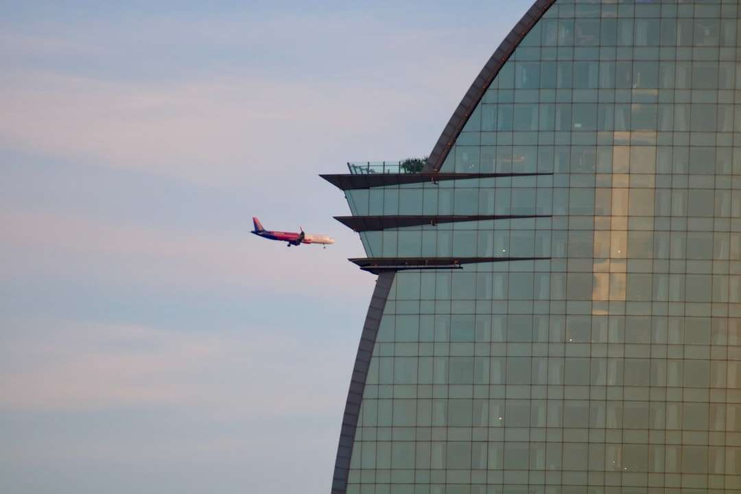 czerwony i biały samolot lecący nad szklanym budynkiem puzzle online