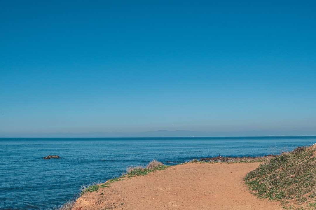 brązowy piasek w pobliżu błękitnego morza pod błękitnym niebem w ciągu dnia puzzle online