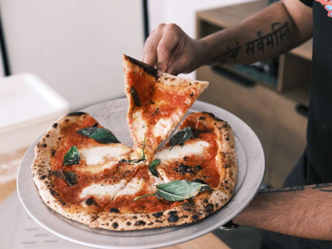 osoba trzymająca pizzę w plasterkach na białym talerzu ceramicznym puzzle online