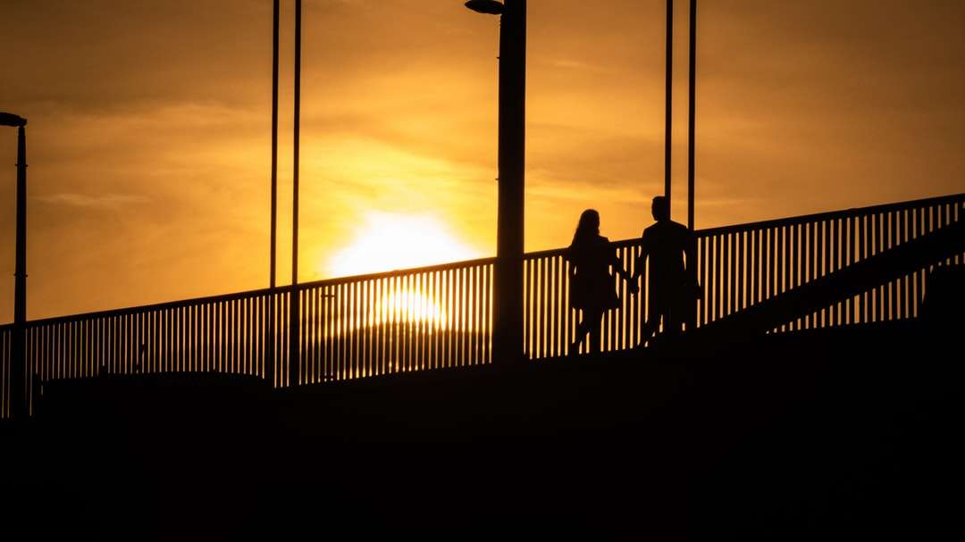 Schattenbild der Leute, die auf Brücke während des Sonnenuntergangs stehen Puzzle