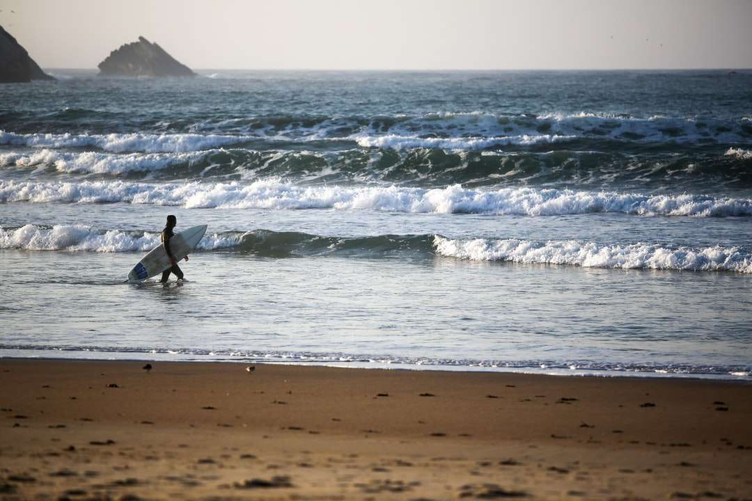 człowiek w czarnym kombinezonie surfing na falach morskich w ciągu dnia puzzle online