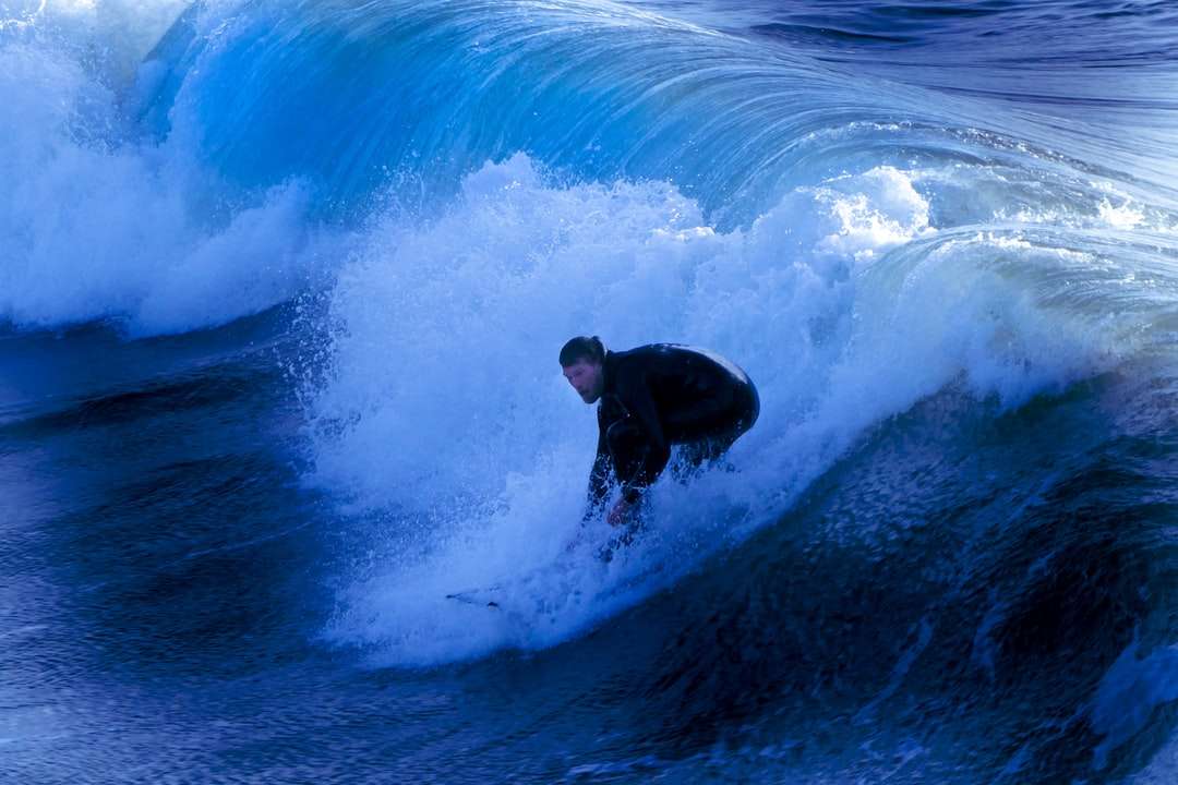 mężczyzna w czarnym kombinezonie surfing na falach błękitnego oceanu puzzle online