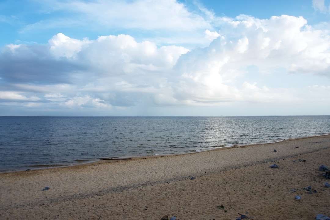 Brązowy piasek blisko ciała wody pod białymi chmurami puzzle online