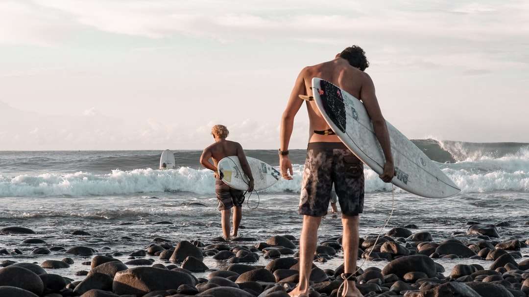 2 kobiety trzyma surfboard stojący na skalistym brzegu puzzle online