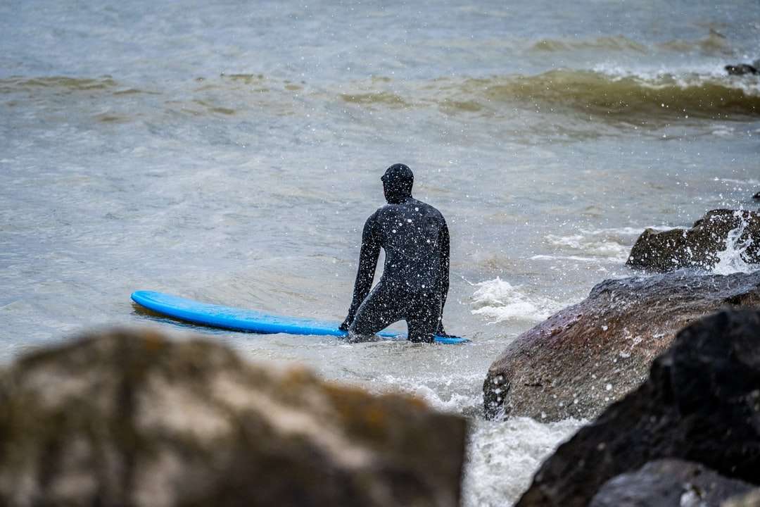 Mężczyzna w czarnym mokrym kostiumu trzyma niebieską deskę surfingową puzzle online