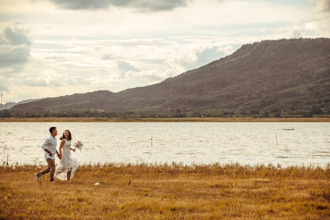 Kobieta w białej sukni obsiadaniu na zielonej trawy polu blisko jeziora puzzle online