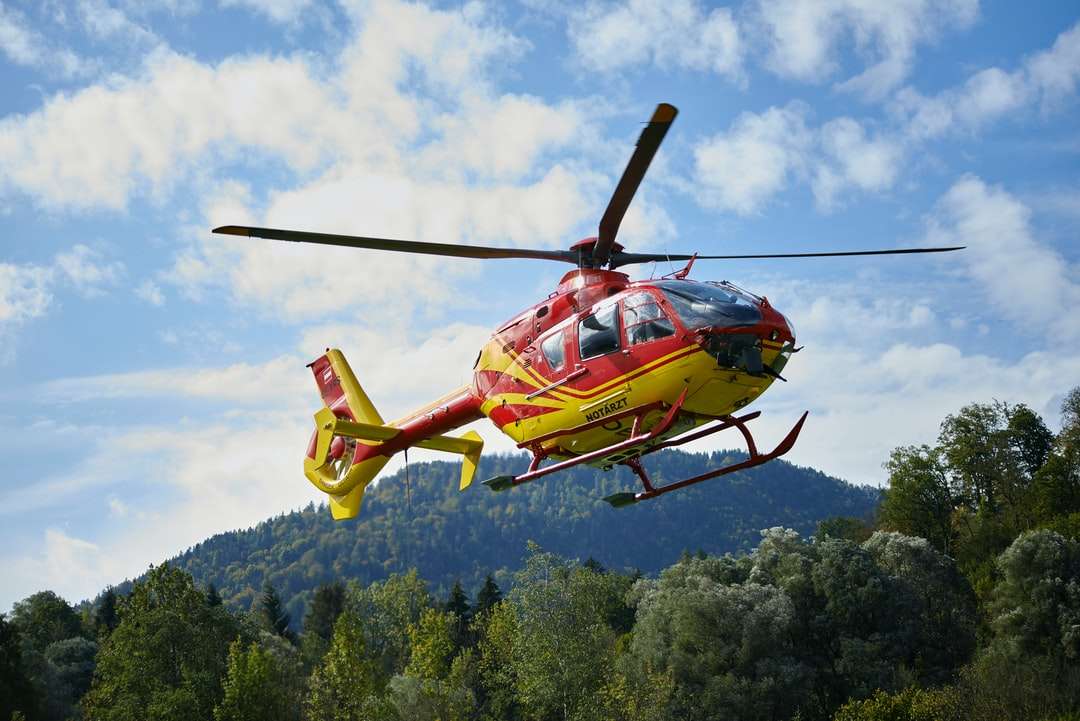 Czerwony i żółty helikopter latający nad zielonymi drzewami puzzle online