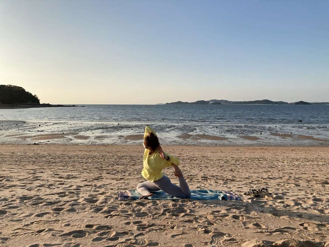 Kobieta w żółtej sukni obsiadaniu na plażowym brzeg podczas dnia puzzle online